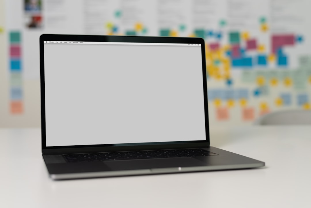 A sleek laptop on a desk with an empty screen and a colorful background of sticky notes and printed paper.